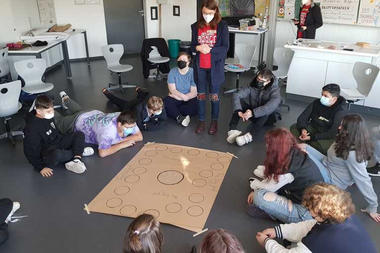 Schüler sitzen im Kreis um Plakat